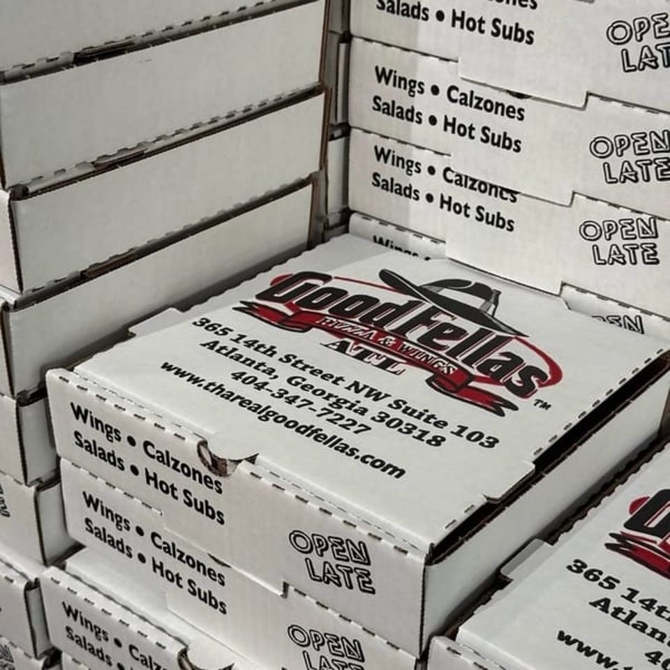 Stacked Foodellas pizza and wings boxes display restaurant branding, Atlanta address, menu items, website, and “Open Late” text.